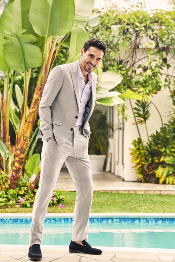 A male Burton model poses in a grey suit with navy loafer shoes and a blue shirt